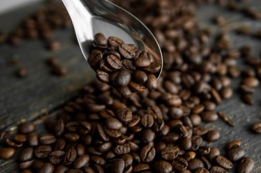 Taze kavrulmuş Arabika kahve çekirdekleri metal kaşıkta ve kahve çekirdekleri ahşap masada serpilmiş..