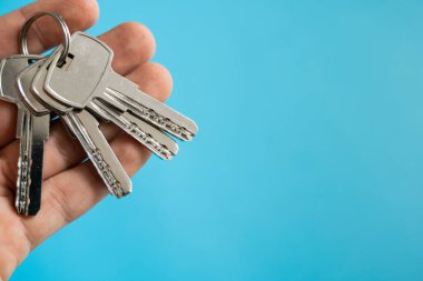 Erkekler mavi arka planı olan bir takım anahtar tutuyorlar. Emlakçıda müşterileri için bir dairenin anahtarı var. Anahtarlara odaklan. Emlakçıların elinde birkaç anahtar..