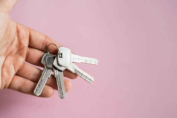 Mens hand holding a set of keys with a pink background. Realtor with a keys to an apartment for a clients. Focus on the keys. Bunch of keys in a realtors hand.