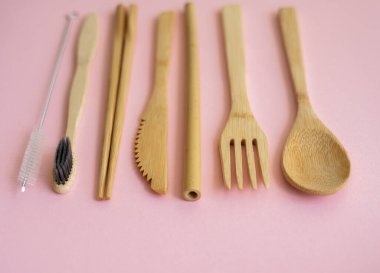 Pembe arka planda bir çantada, çevre dostu bambu çatal bıçak seti. Sıfır atık. Masanın üzerinde duran bir çantanın içindeki bambu çatal bıçak seti. Kaşık, çatal, bıçak, diş fırçası, tüp ve Çin çubukları..