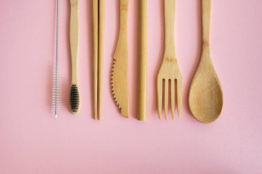 Pembe arka planda bir çantada, çevre dostu bambu çatal bıçak seti. Sıfır atık. Masanın üzerinde duran bir çantanın içindeki bambu çatal bıçak seti. Kaşık, çatal, bıçak, diş fırçası, tüp ve Çin çubukları..