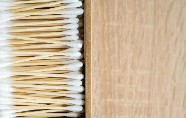 Eco-friendly cotton swabs. A cardboard box containing recyclable bamboo cotton buds on a table. Zero waste concept. Eco product. Cosmetic sticks in a box. Wooden sticks for cleaning ears.