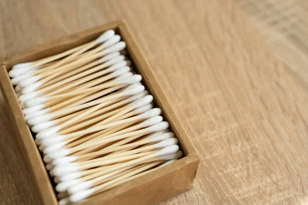Eco-friendly cotton swabs. A cardboard box containing recyclable bamboo cotton buds on a table. Zero waste concept. Eco product. Cosmetic sticks in a box. Wooden sticks for cleaning ears.