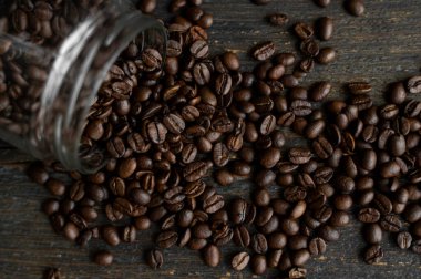 Ahşap bir masadaki küçük bir kavanozdan masaya serpilmiş kavrulmuş taze Arap kahve çekirdekleri. Taze kahve çekirdekleri.