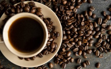 Ahşap masa arkasında kavrulmuş kahve çekirdekli kahve fincanı. Bir kupa sade kahve ve ahşap bir masanın üzerinde kahve çekirdekleri. Taze kahve çekirdekleri.