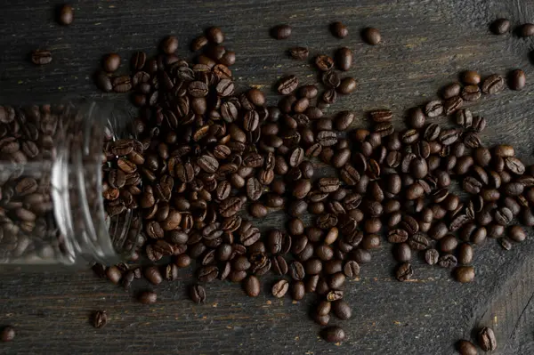 Смажені свіжі арабіки кавові зерна розкидані на столі з маленької банки на дерев'яному столі. Свіжі кавові зерна . — стокове фото