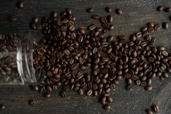 Grãos de café arábica frescos assados espalhados em uma mesa de um pequeno jarro em uma mesa de madeira. Grãos de café frescos. — Fotografia de Stock