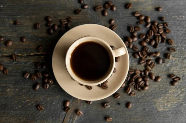 커피 잔에 볶은 커피 원두를 나무로 된 테이블 배경 위에 놓는다. 나무 탁자 위에는 커피 원두가 흩어져 있는 검은 커피 덩어리가 있었다. 신선 한 커피 콩. — 스톡 사진