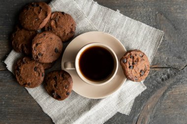 Ahşap masa arkasında kurabiyeler olan kahve fincanı. Bir fincan sade kahve ve çikolatalı kurabiye. Taze kahve çekirdekleri.