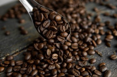 Taze kavrulmuş Arabika kahve çekirdekleri metal kaşıkta ve kahve çekirdekleri ahşap masada serpilmiş..