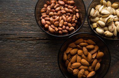 Badem, şam fıstığı ve küçük bir tabakta yer fıstığı. Siyah bir masanın üzerinde duruyorlar. Fındık sağlıklı bir vejetaryen proteini ve besleyici yemektir..