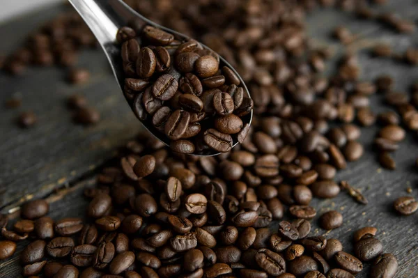 Taze kavrulmuş Arabika kahve çekirdekleri metal kaşıkta ve kahve çekirdekleri ahşap masada serpilmiş..