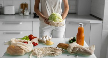 Yeniden kullanılabilir ekolojik market poşeti sebzeli ve lahanalı kadın elini tutuyor. Sıfır atık ve plastiksiz konsept. Kız elinde sebzeli pamuk alıcısı tutuyor..