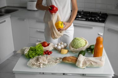 Yeniden kullanılabilir ekolojik markette sebzeli el ele tutuşan kadın kırmızı ve sarı biberi çıkardı. Sıfır atık ve plastiksiz konsept. Kız elinde sebzeli pamuk alıcısı tutuyor..