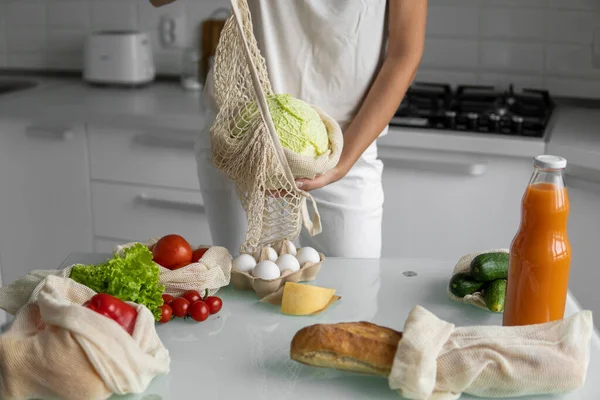 Mano de mujer sosteniendo la bolsa de comestibles eco textil reutilizable con verduras y saca cabaña. Cero residuos y concepto libre de plástico. Chica está sosteniendo malla de algodón shopper con verduras. — Foto de Stock