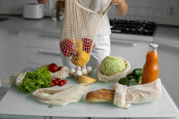 Yeniden kullanılabilir ekolojik markette sebzeli el ele tutuşan kadın kırmızı ve sarı biberi çıkardı. Sıfır atık ve plastiksiz konsept. Kız elinde sebzeli pamuk alıcısı tutuyor..