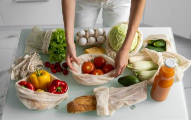 Yeniden kullanılabilir ekolojik markette sebzeli el ele tutuşan ve kırmızı domatesi dışarı çıkaran kadın. Sıfır atık ve plastiksiz konsept. Kız elinde sebzeli pamuk alıcısı tutuyor..