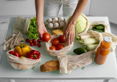Yeniden kullanılabilir ekolojik markette sebzeli el ele tutuşan ve kırmızı domatesi dışarı çıkaran kadın. Sıfır atık ve plastiksiz konsept. Kız elinde sebzeli pamuk alıcısı tutuyor..