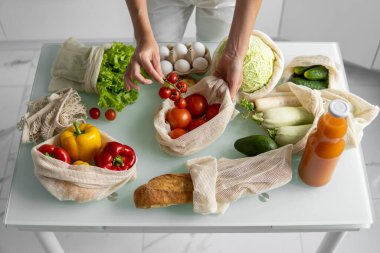 Yeniden kullanılabilir ekolojik markette sebzeli el ele tutuşan ve kırmızı domatesi dışarı çıkaran kadın. Sıfır atık ve plastiksiz konsept. Kız elinde sebzeli pamuk alıcısı tutuyor..
