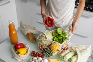 Yeniden kullanılabilir ekolojik markette sebzeli el ele tutuşan kadın kırmızı ve sarı biberi çıkardı. Sıfır atık ve plastiksiz konsept. Kız elinde sebzeli pamuk alıcısı tutuyor..