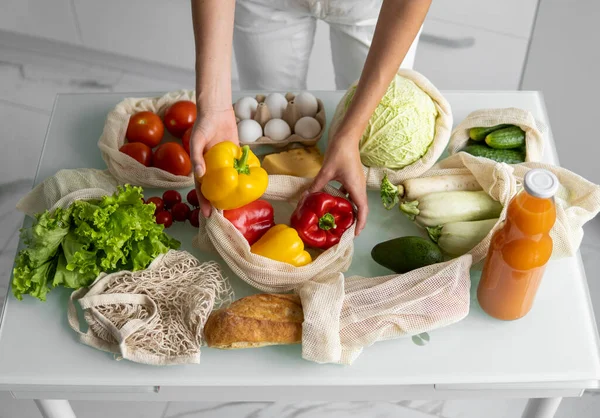 Woman hand holding Reusable eco textile grocery bag with vegetables and takes red and yellow pepper out. Zero waste and plastic free concept. Girl is holding mesh cotton shopper with vegetables. — Stock Photo, Image