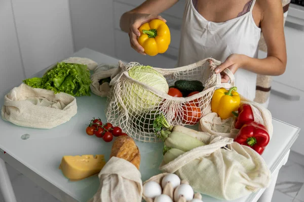 Vrouw hand houden Herbruikbare eco textiel kruidenierszakje met groenten en neemt rode en gele peper uit. Geen afval en plastic vrij concept. Meisje houdt mesh katoen shopper met groenten. — Stockfoto