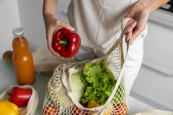 Vrouw hand houden Herbruikbare eco textiel kruidenierszakje met groenten en neemt rode en gele peper uit. Geen afval en plastic vrij concept. Meisje houdt mesh katoen shopper met groenten. — Stockfoto