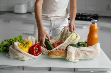 Yeniden kullanılabilir ekolojik markette sebzeli ve salatalıklı el ele tutuşan kadın. Sıfır atık ve plastiksiz konsept. Kız elinde sebzeli pamuk alıcısı tutuyor..