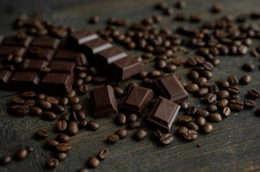 Kavrulmuş Arap kahve çekirdekleri bir çubuk koyu çikolatayla ahşap masaya saçılmış. Taze kahve çekirdekleri.