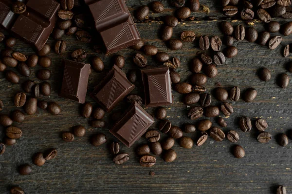 아라 비카 커피 원두는 어두운 초콜릿바가 있는 나무 탁자 위에 흩어져 있다. 신선 한 커피 콩. — 스톡 사진
