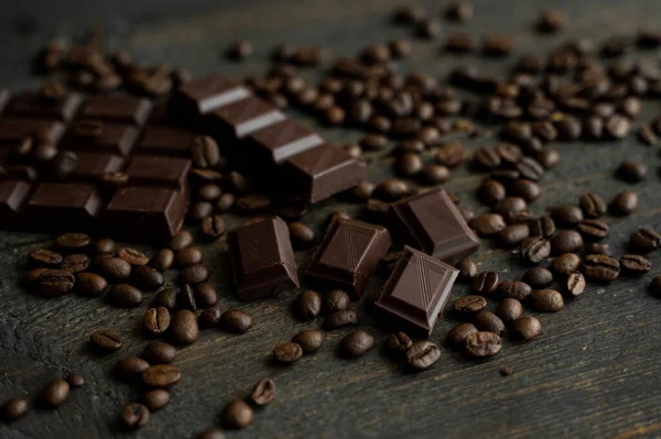 Kavrulmuş Arap kahve çekirdekleri bir çubuk koyu çikolatayla ahşap masaya saçılmış. Taze kahve çekirdekleri.