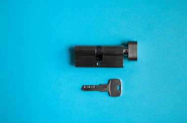 Mavi arka planda anahtarı olan bir kapı kilidi silindiri. Kilidin silindiri anahtarla. Kapıya yeni bir kilit takıyorum. Kapı için yedek parça..