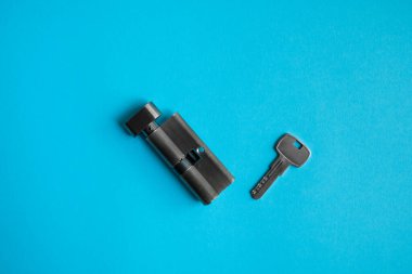 Mavi arka planda anahtarı olan bir kapı kilidi silindiri. Kilidin silindiri anahtarla. Kapıya yeni bir kilit takıyorum. Kapı için yedek parça..