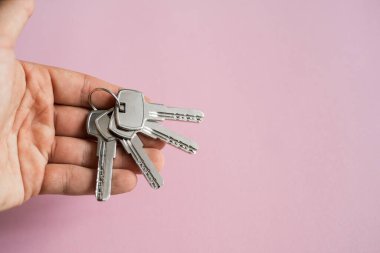 Erkekler pembe arka planı olan bir takım anahtar tutuyorlar. Emlakçıda müşterileri için bir dairenin anahtarı var. Anahtarlara odaklan. Emlakçıların elinde birkaç anahtar..