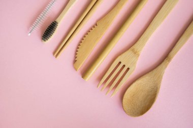 Pembe arka planda bir çantada, çevre dostu bambu çatal bıçak seti. Sıfır atık. Masanın üzerinde duran bir çantanın içindeki bambu çatal bıçak seti. Kaşık, çatal, bıçak, diş fırçası, tüp ve Çin çubukları..