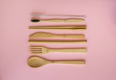 Pembe arka planda bir çantada, çevre dostu bambu çatal bıçak seti. Sıfır atık. Masanın üzerinde duran bir çantanın içindeki bambu çatal bıçak seti. Kaşık, çatal, bıçak, diş fırçası, tüp ve Çin çubukları..