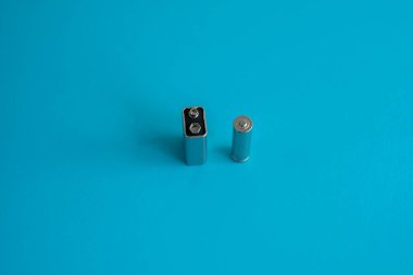 Yüksek voltajlı Volt 9V pil ve mavi arka planda alkali AA batarya. Enerji.