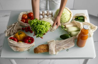 Kadın eli, evde sebzeli tekrar kullanılabilir bir poşet tutuyor ve salatayı dışarı çıkarıyor. Sıfır atık ve plastiksiz konsept. Sebzeli pamuk satıcısı. Ekoloji.