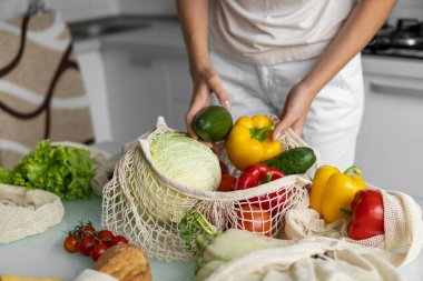 Kadın marketten döndü ve evdeki bir mutfakta sebze dolu bir poşeti açtı. Sıfır atık ve plastiksiz konsept. Kız elinde sebzeli pamuk alıcısı tutuyor..