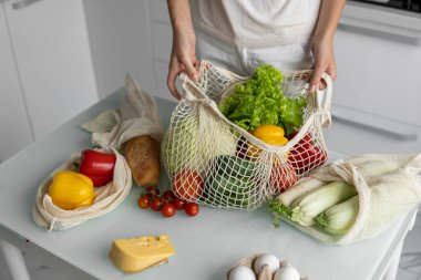 Kadın marketten döndü ve evdeki bir mutfakta sebze dolu bir poşeti açtı. Sıfır atık ve plastiksiz konsept. Kız elinde sebzeli pamuk alıcısı tutuyor..