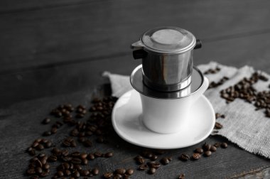 Üstünde metal filtre olan beyaz bir fincan kahve ve ahşap bir masanın üzerine serpiştirilmiş fasulye. Geleneksel Vietnam kahvesi..