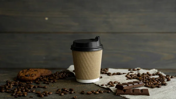 Papieren kopje koffie met gebrande koffiebonen op houten tafel. Mok zwarte koffie met koekjes en chocolade op tafel. — Stockfoto
