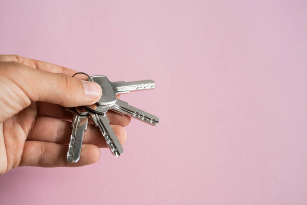 Mens hand holding a set of keys with a pink background. Realtor with a keys to an apartment for a clients. Focus on the keys. Bunch of keys in a realtors hand.