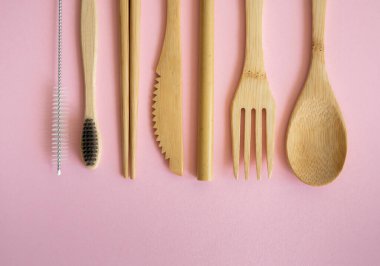 Pembe arka planda bir çantada, çevre dostu bambu çatal bıçak seti. Sıfır atık. Masanın üzerinde duran bir çantanın içindeki bambu çatal bıçak seti. Kaşık, çatal, bıçak, diş fırçası, tüp ve Çin çubukları..