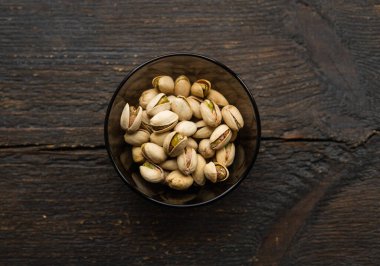 Eski ahşap bir masada küçük bir tabakta şam fıstığı. Pistachio sağlıklı bir vejetaryen protein yiyeceğidir. Doğal çerezler.