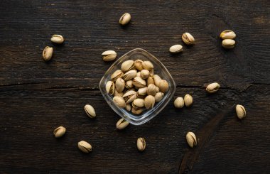 Arka plan olarak eski ahşap bir masada, bir tabağın etrafına saçılmış badem cevizleri olan küçük bir tabakta şam fıstığı. Pistachio sağlıklı bir vejetaryen protein yiyeceğidir. Doğal çerezler.