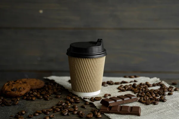 Paper cup of coffee with roasted coffee beans on wooden table. Mug of black coffee with a cookies and chocolate on a table. — Stock Photo, Image