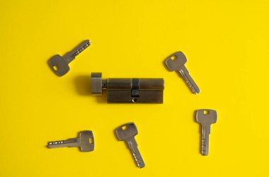 Sarı arka planda anahtarları olan bir kapı kilidi silindiri. Anahtarlı kilidin silindiri. Kapıya yeni bir kilit takıyorum. Kapı için yedek parça..