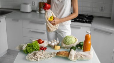 Kadın eli, evde sebzeli ve tekrar kullanılabilir bir market poşeti tutuyor ve biberi çıkarıyor. Sıfır atık ve plastiksiz konsept. Sebzeli pamuk satıcısı. Ekoloji.