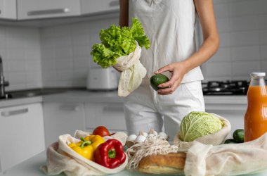 Kadın eli, evde sebzeli tekrar kullanılabilir bir poşet tutuyor ve salata ile avokadoyu dışarı çıkarıyor. Sıfır atık ve plastiksiz konsept. Sebzeli pamuk satıcısı. Ekoloji.